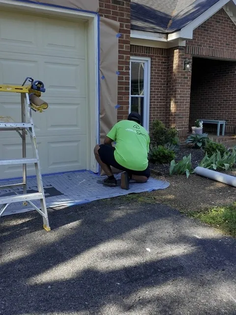 A Hisway painter kneeling on a floor cover, masking a garage door