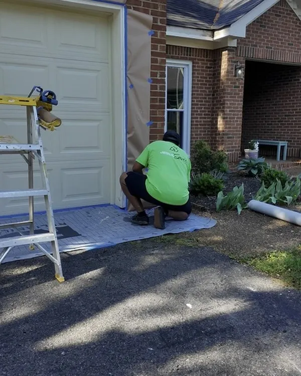A Hisway painter kneeling on a floor cover, masking a garage door