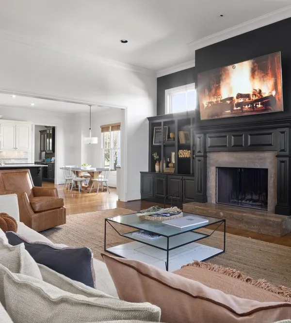 A finished family room with painted black built-ins and a white kitchen beyond