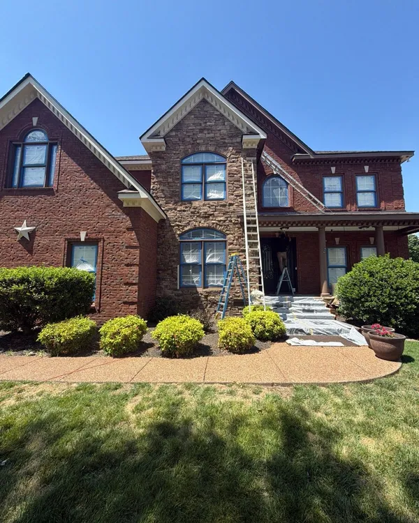 A brick home with windows masked in plastic, the porch steps covered and ladders up
