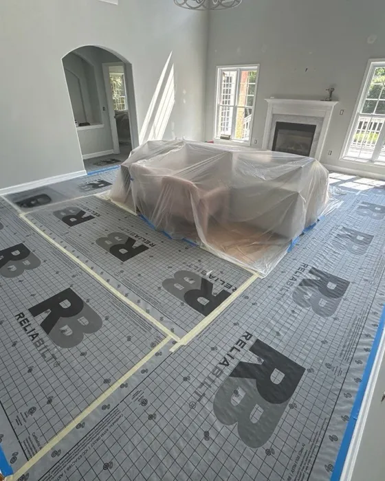 A living room with the floor covered in synthetic underlayment, the edges taped and the sofa wrapped in clear plastic